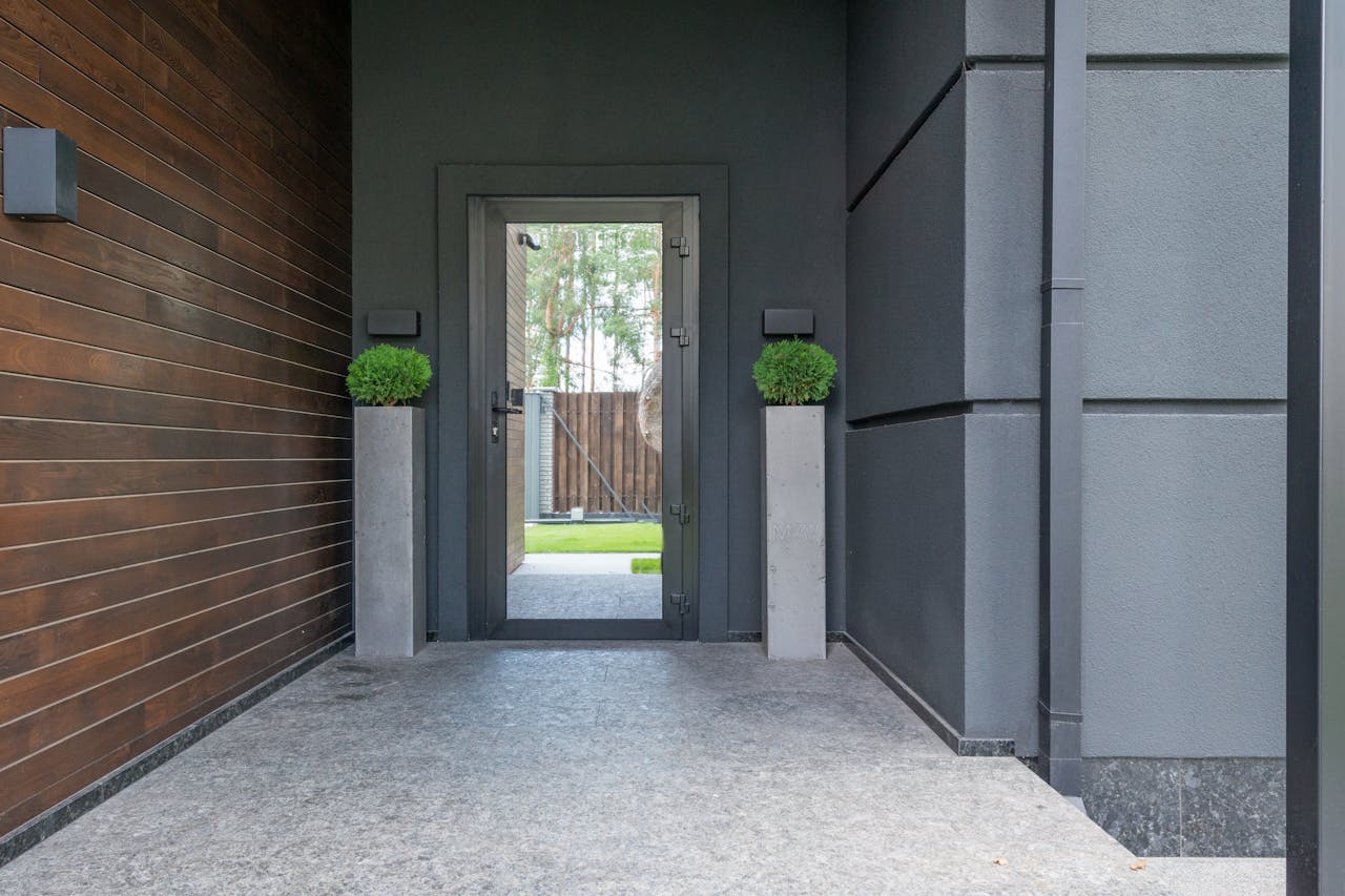 about-01 Contemporary entrance featuring a glass door, wooden walls, and elegant potted plants.