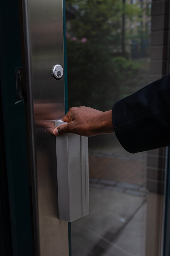 service-01 Close-up of a hand pushing open a modern glass door with a metal handle.